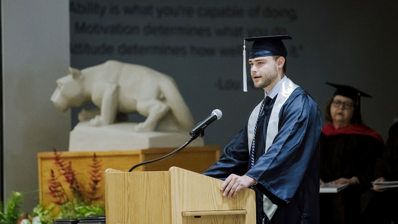 Male student in cap and gown giving a speech at commencement.