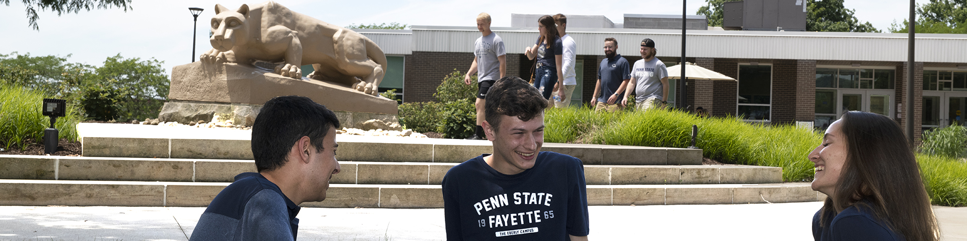 Several students sitting in front of the lion shrine and others walking behind the shrine. 