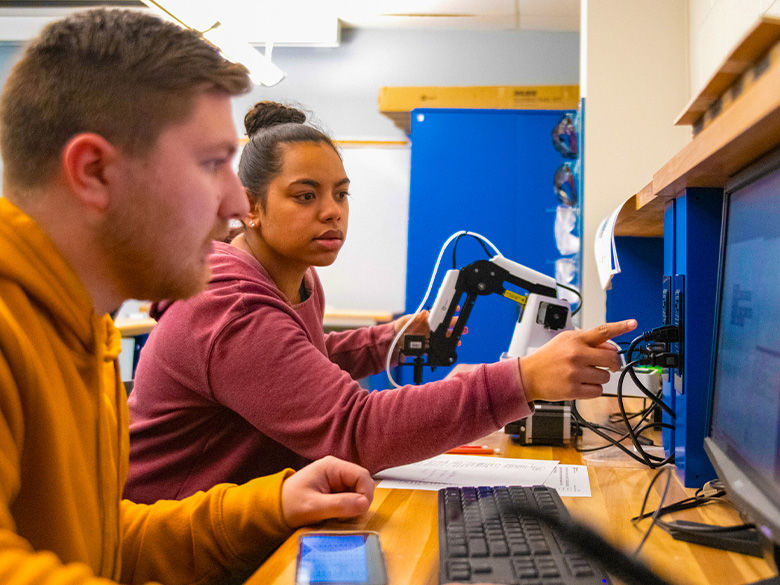 A student working on computers alongside her class mate.