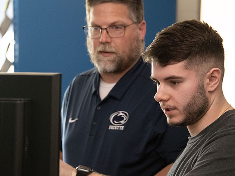 Student asking a professor a question with a computer screen in front of them.