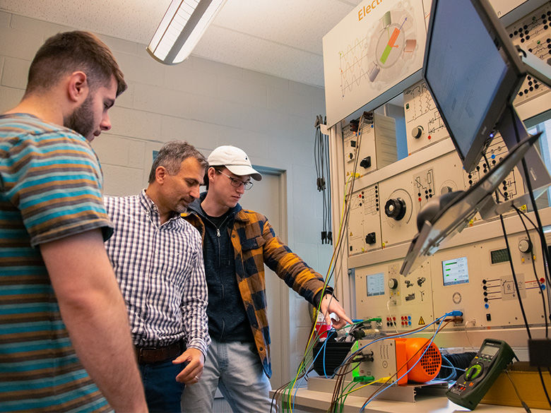 Two students working with a professor on an electrical system.