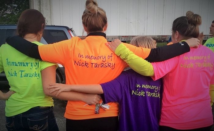 A group poses with their backs to the camera; their t-shirts read "In memory of Nick Tarasky"