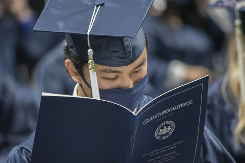 graduate in cap, gown, and face mask reading program