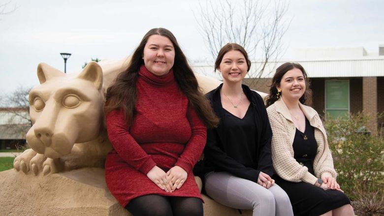 Three Nittany Lions Read and Count student workers sitting next to the Nittany Lion shrine