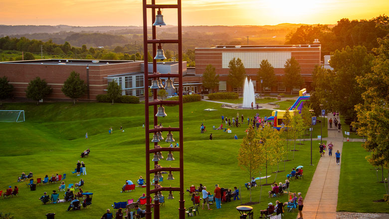 The campus belltower at sunset; beneath it are visitors walking around campus.