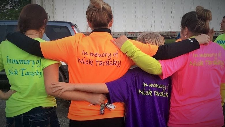 A group poses with their backs to the camera; their t-shirts read "In memory of Nick Tarasky"