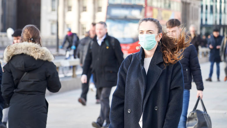Several people walk along a busy city street. Some have on face masks, others do not.