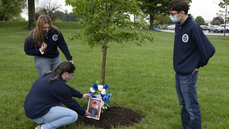 From left to right: Maria Catalina, Alexis Williams, and Jacob Levendosky place a wreath at the memorial tree for Brandon Peterson.