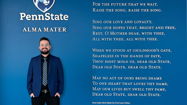 Joshua Krause standing beside the Alma Mater lyrics display at the HUB-Robeson Center.