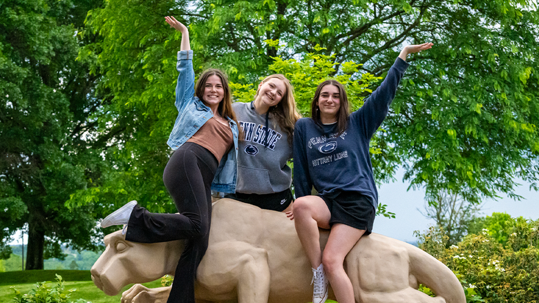 Three students posing cheerfully against the Fayette campus' lion shrine.