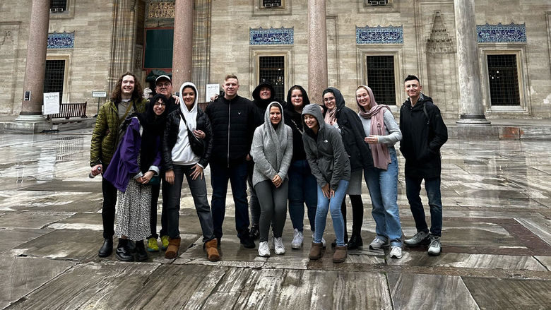 Students gathering with faculty and guests in front of the beautiful Turkish architecture. 