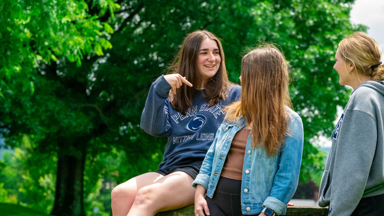 Three students talking outside; trees are behind them.