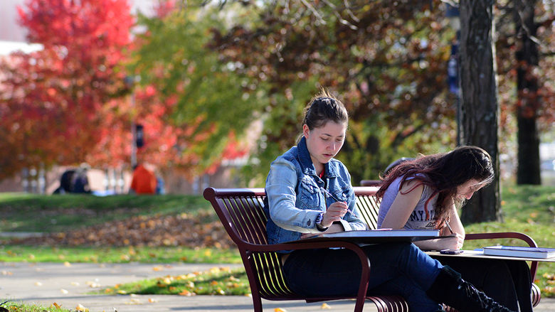 Two students painting outside on a bench.