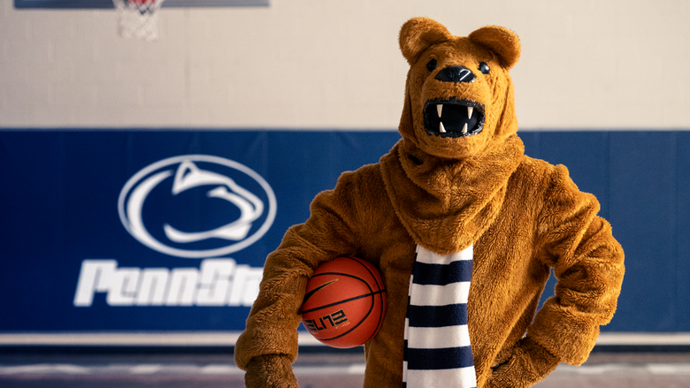 The Nittany Lion mascot stands on the court with a basketbal at their waist.
