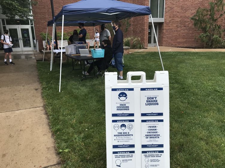 Penn State employees stand under a tent to register sport camp participants for the day. 