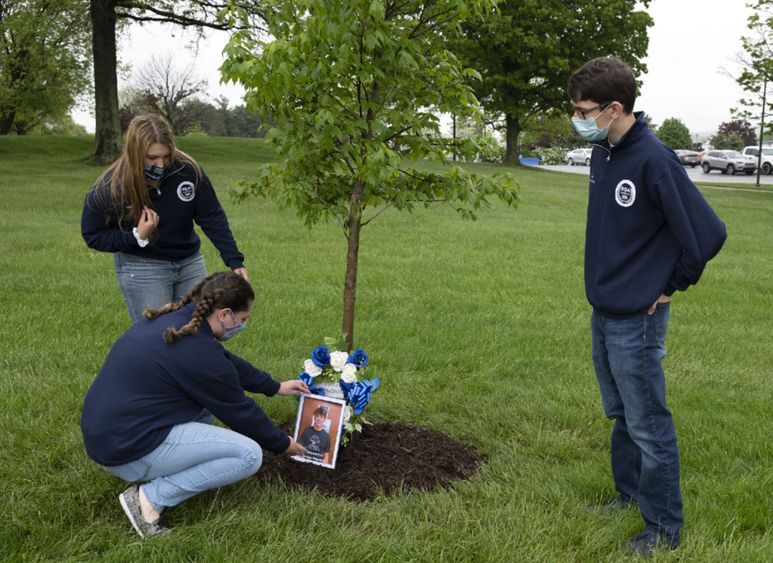 From left to right: Maria Catalina, Alexis Williams, and Jacob Levendosky place a wreath at the memorial tree for Brandon Peterson.